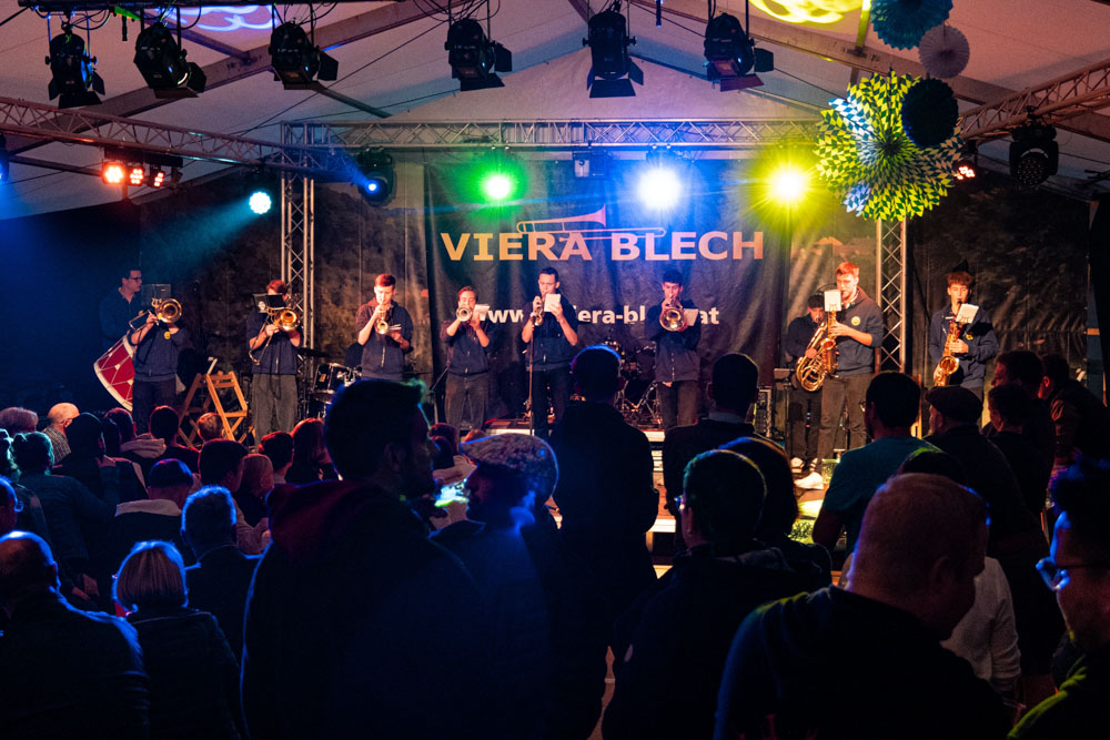 Die Blasmusik-Band Fetz-Blech spielt live auf einer bunt beleuchteten Konzertbühne vor Publikum.